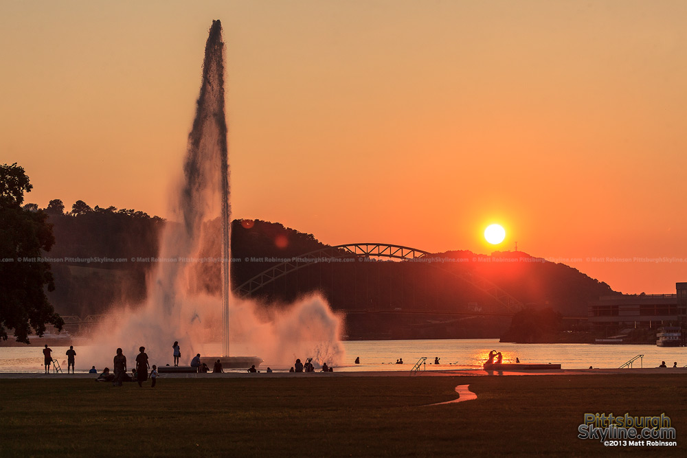 The sun sets over the Ohio River with the fountain at the Point